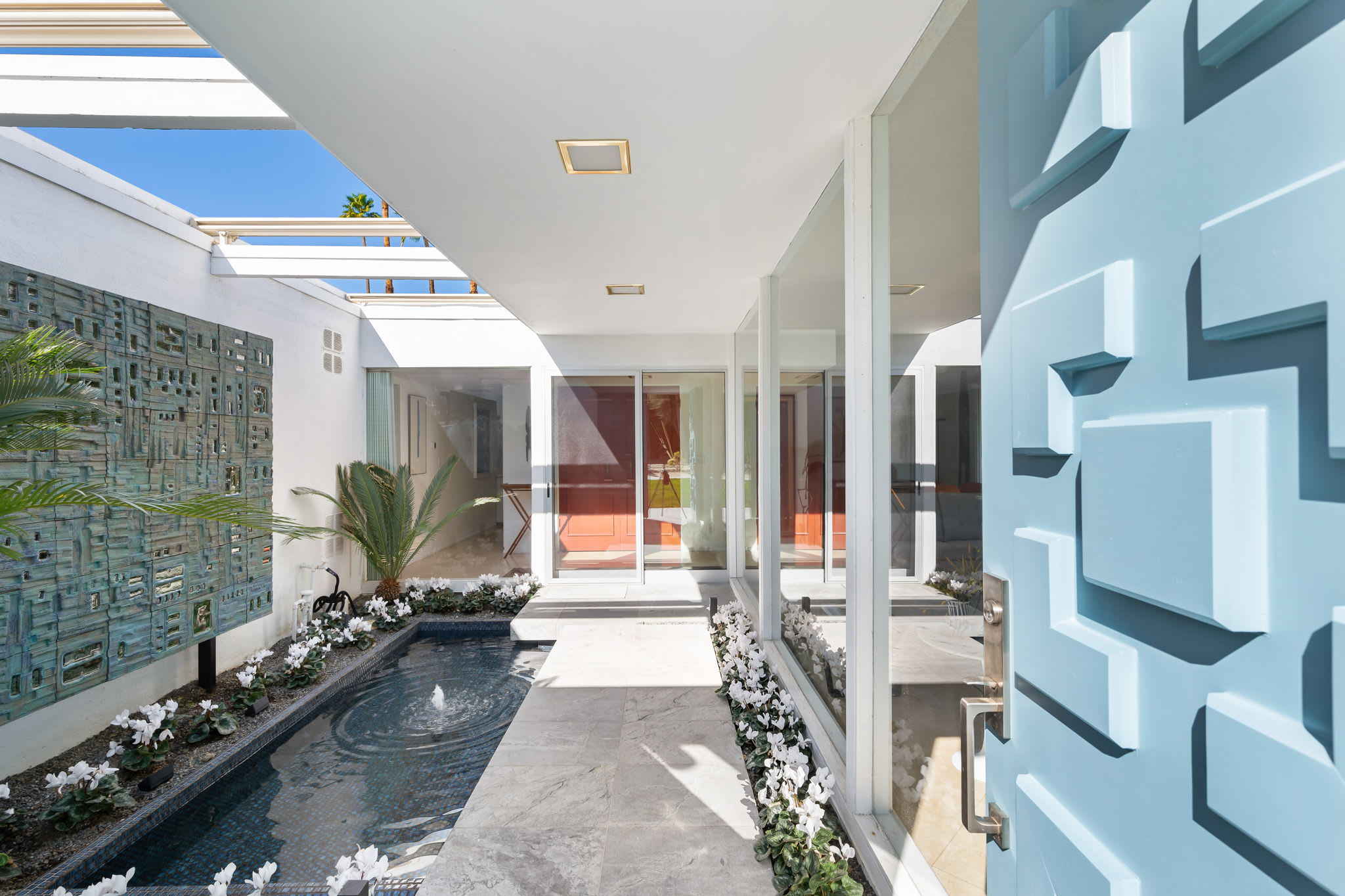 Front courtyard with a blue geometric gate, planted border and covered walkway.