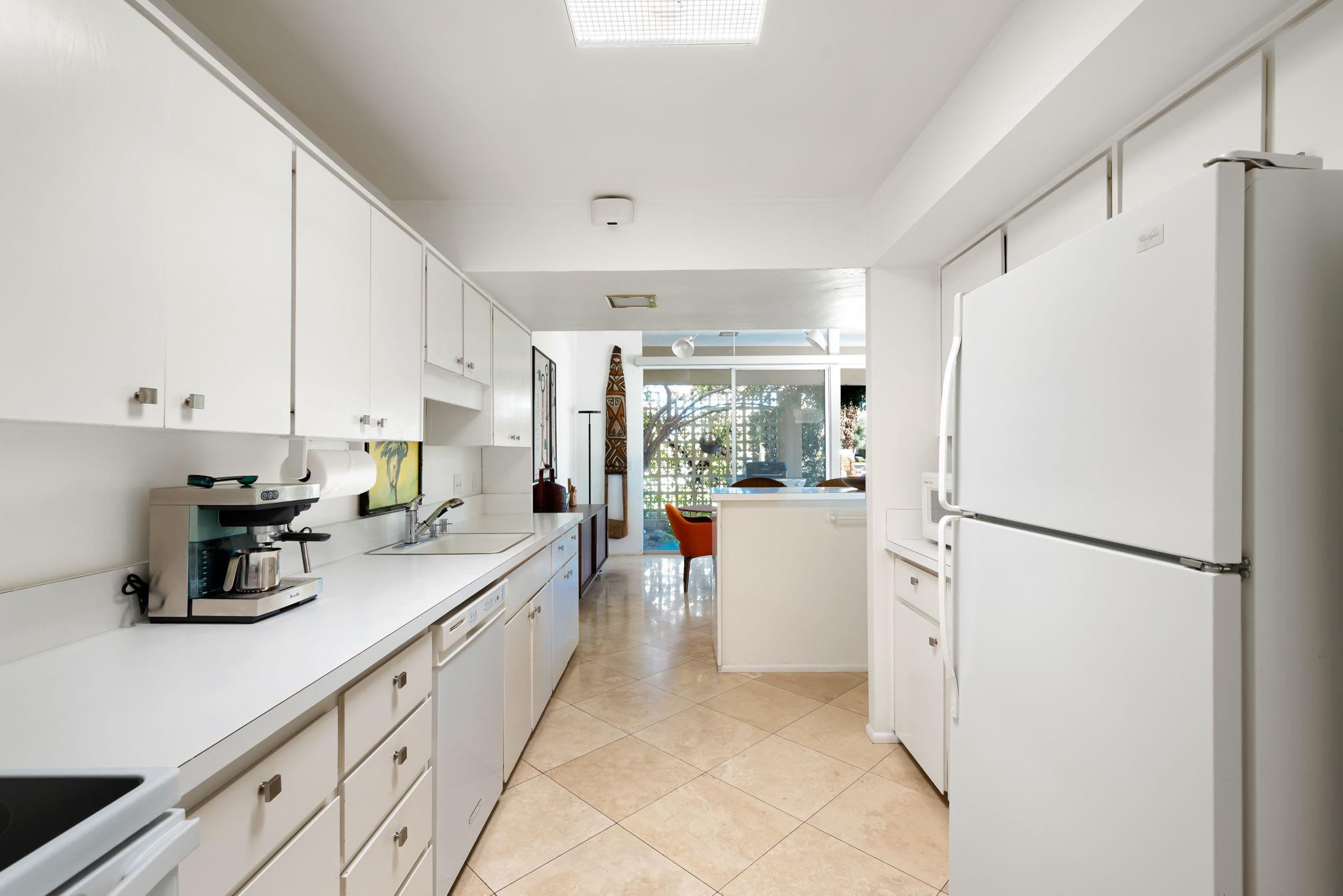 Galley kitchen with white cabinetry, refrigerator and countertop appliances.