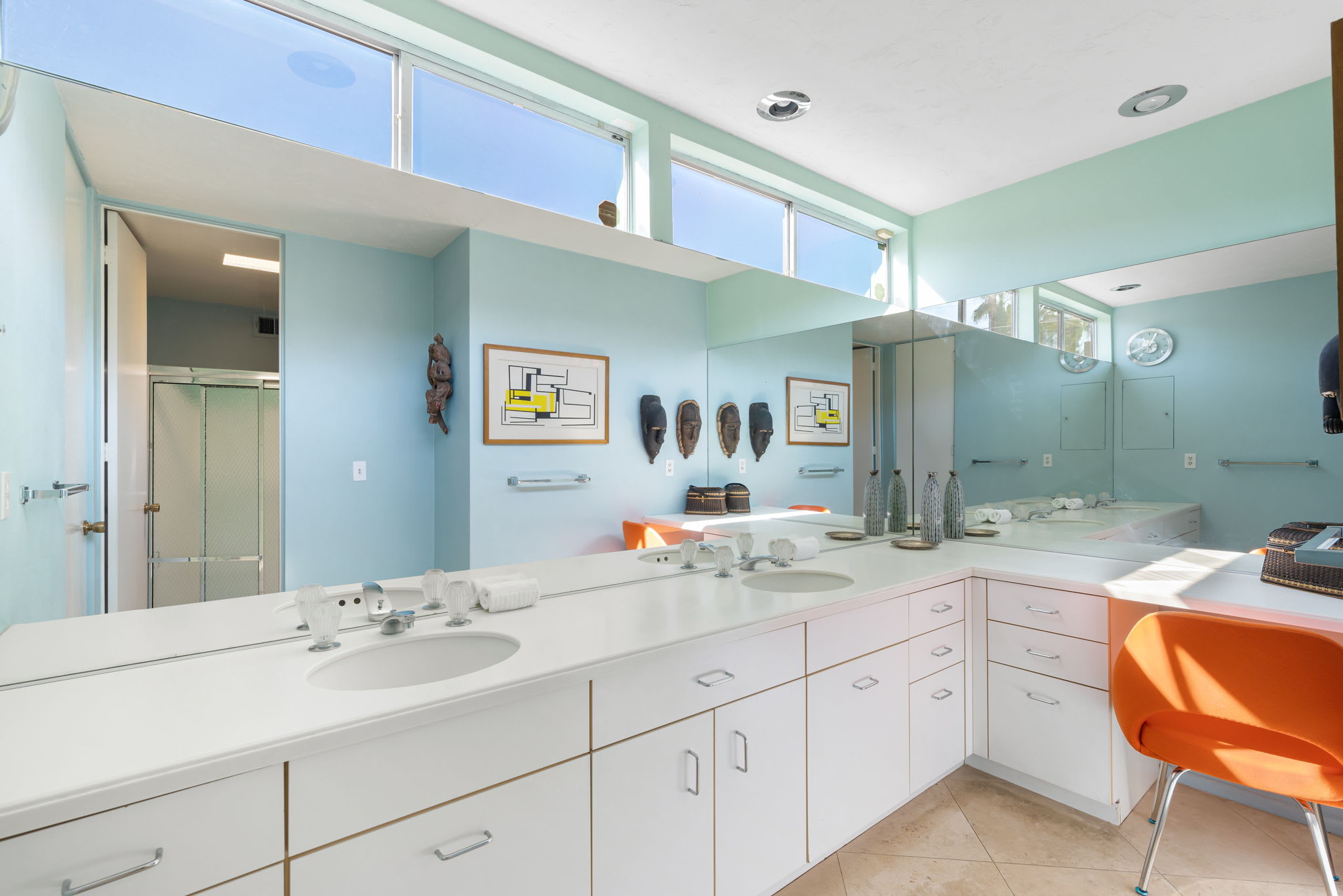 Bathroom with a long mirrored vanity, double sinks and a glass shower.