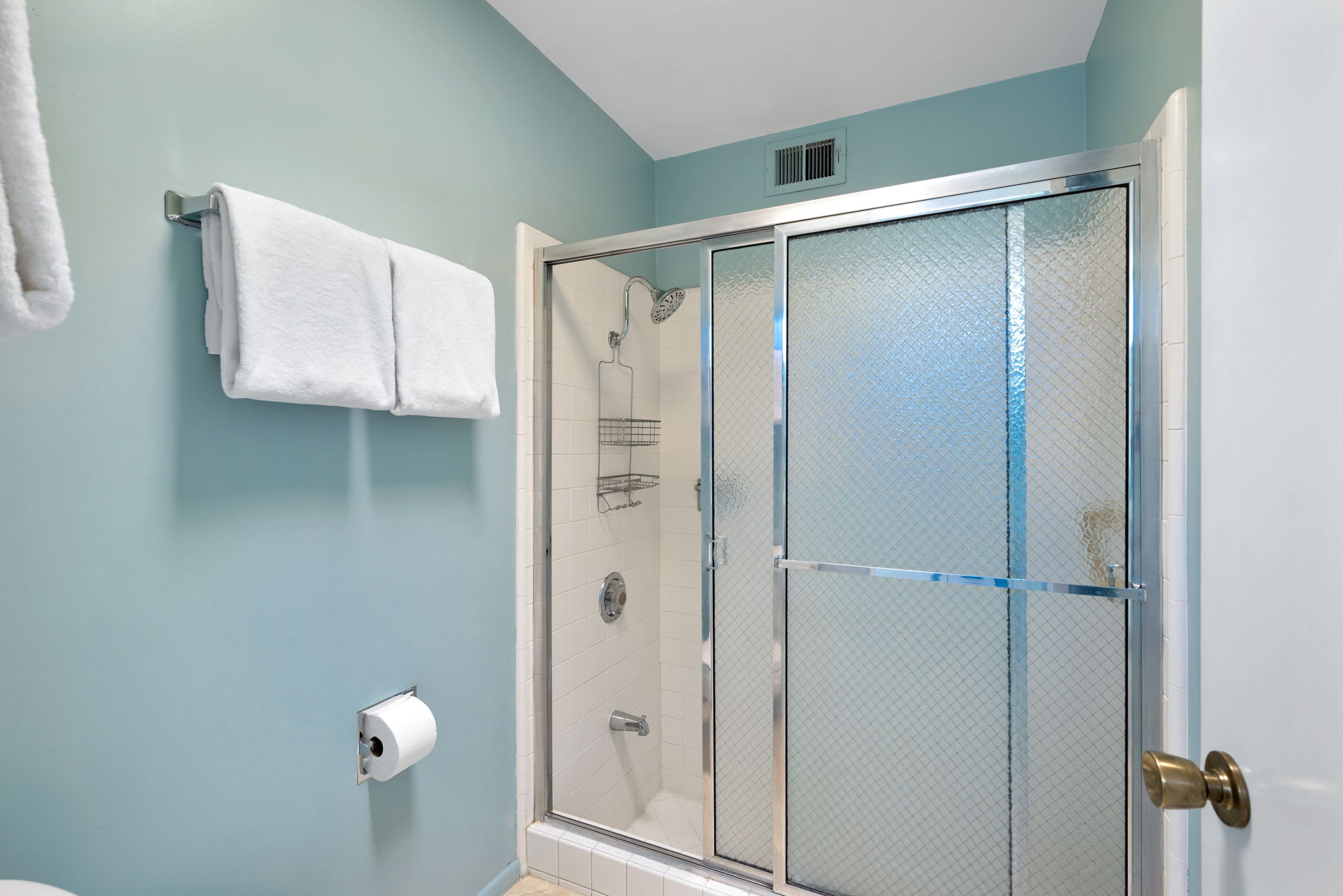 Bathroom with a glass shower, blue walls and hanging towels.
