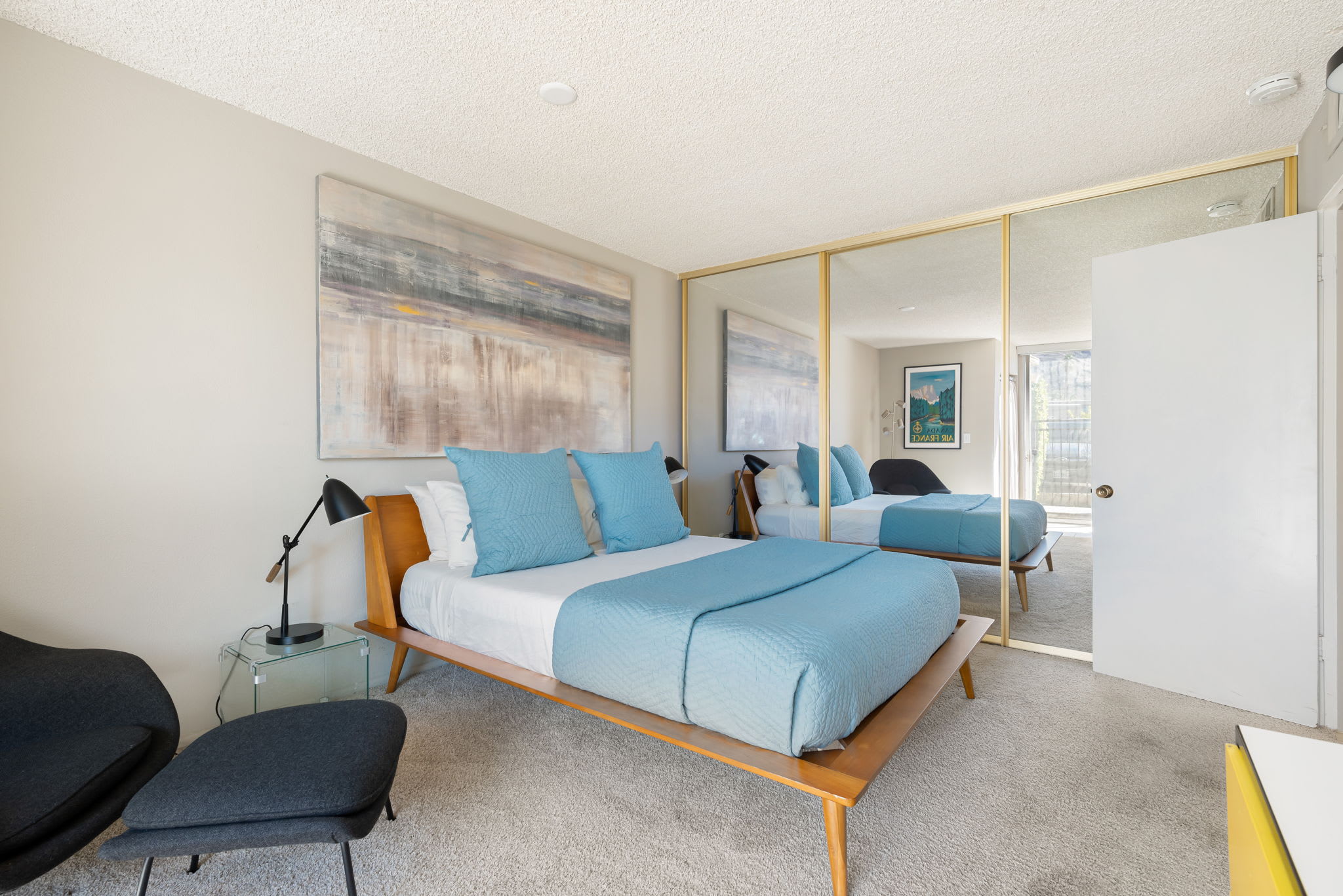 Bedroom with blue bedding, bedside lamps and mirrored closet doors.