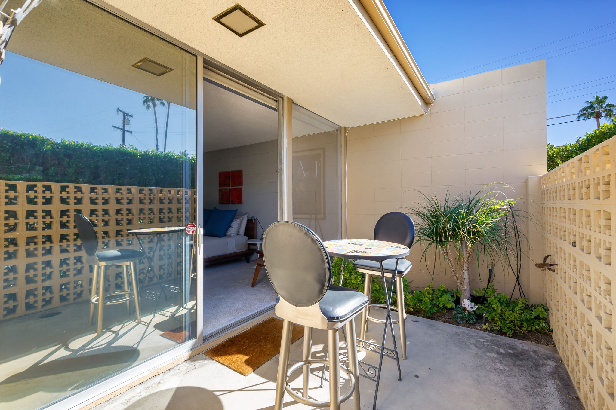 Covered porch seating beside a door and patterned privacy wall.