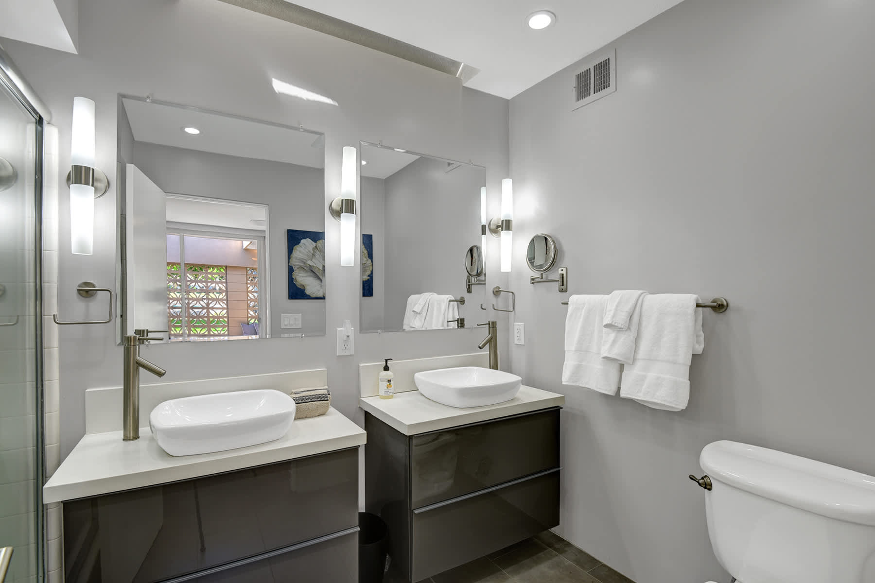 Bathroom with a double vanity, mirrors, storage cabinets and toilet.