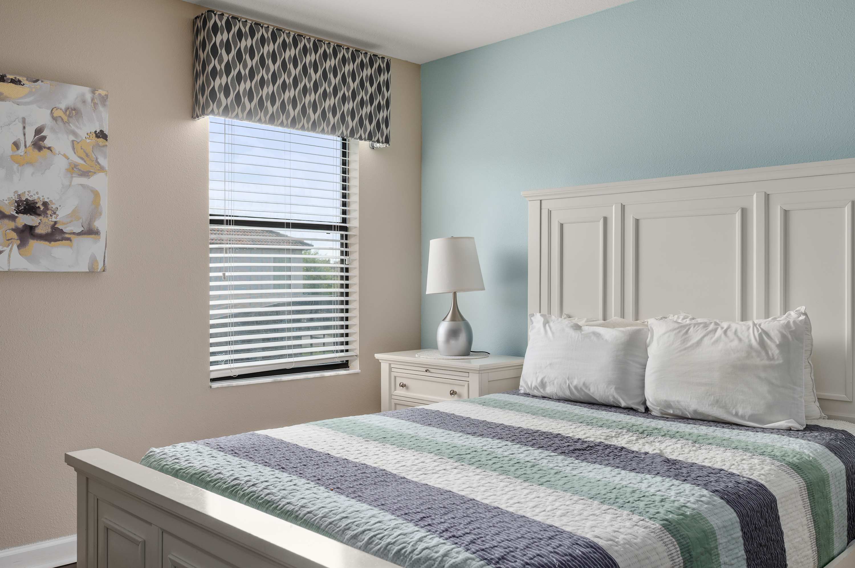 Peaceful bedroom w/ soft blue walls, striped bedding & natural light