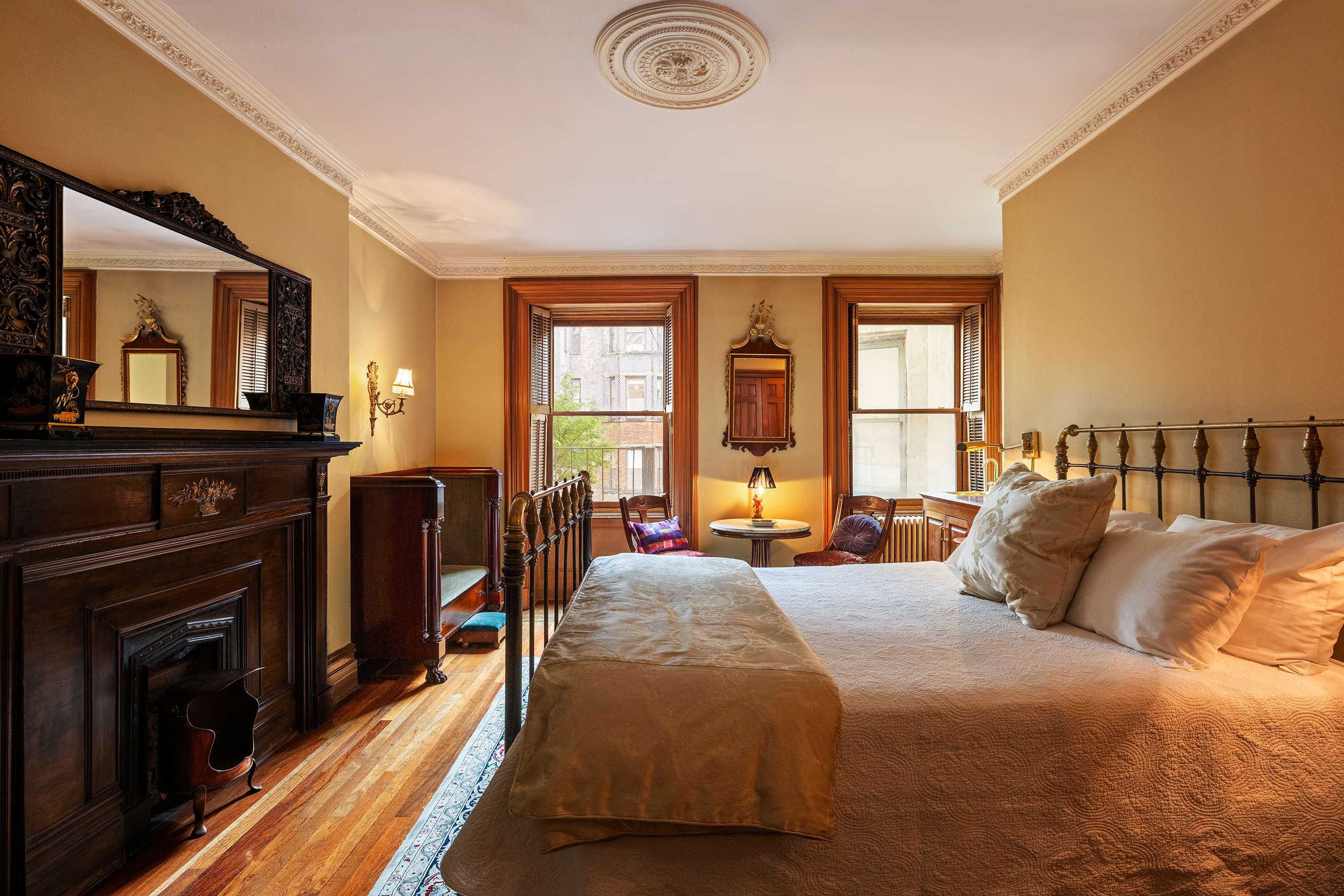A wide-angle view of a bedroom with a large bed, a fireplace, and two windows.