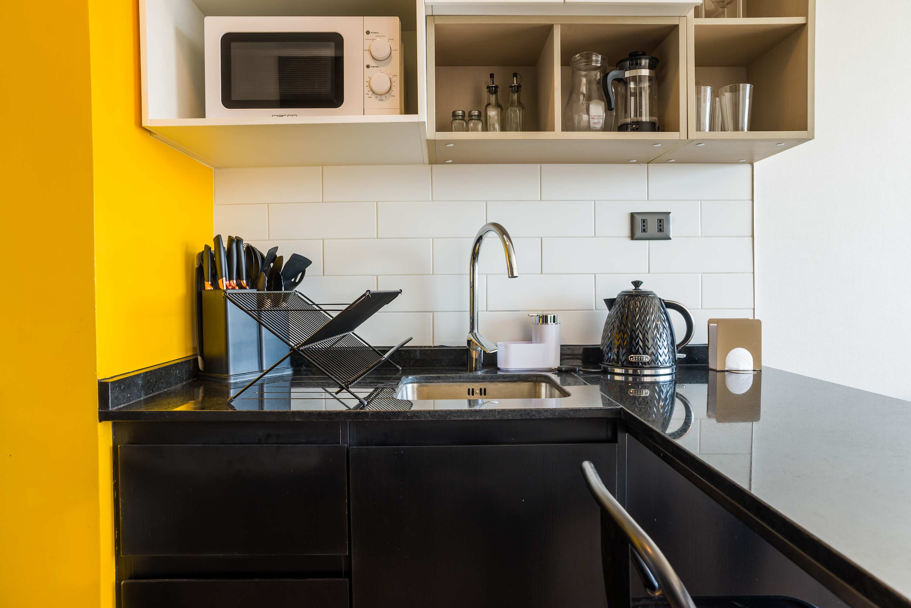 Modern kitchenette with sleek black countertops and vibrant yellow accents, perfect for quick meals and morning coffee.