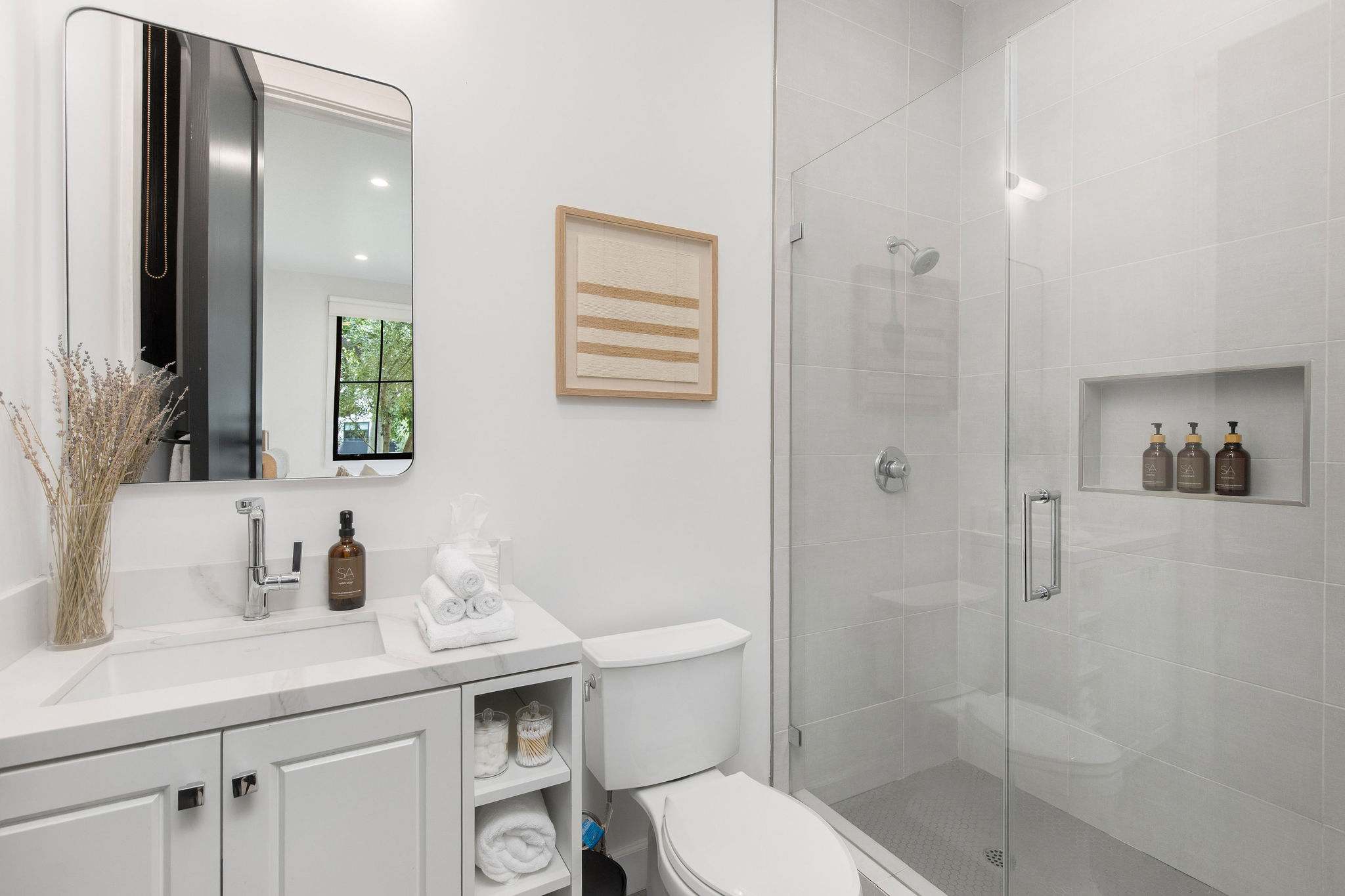 A full bathroom with walk-in glass shower, built-in storage, and contemporary detailing