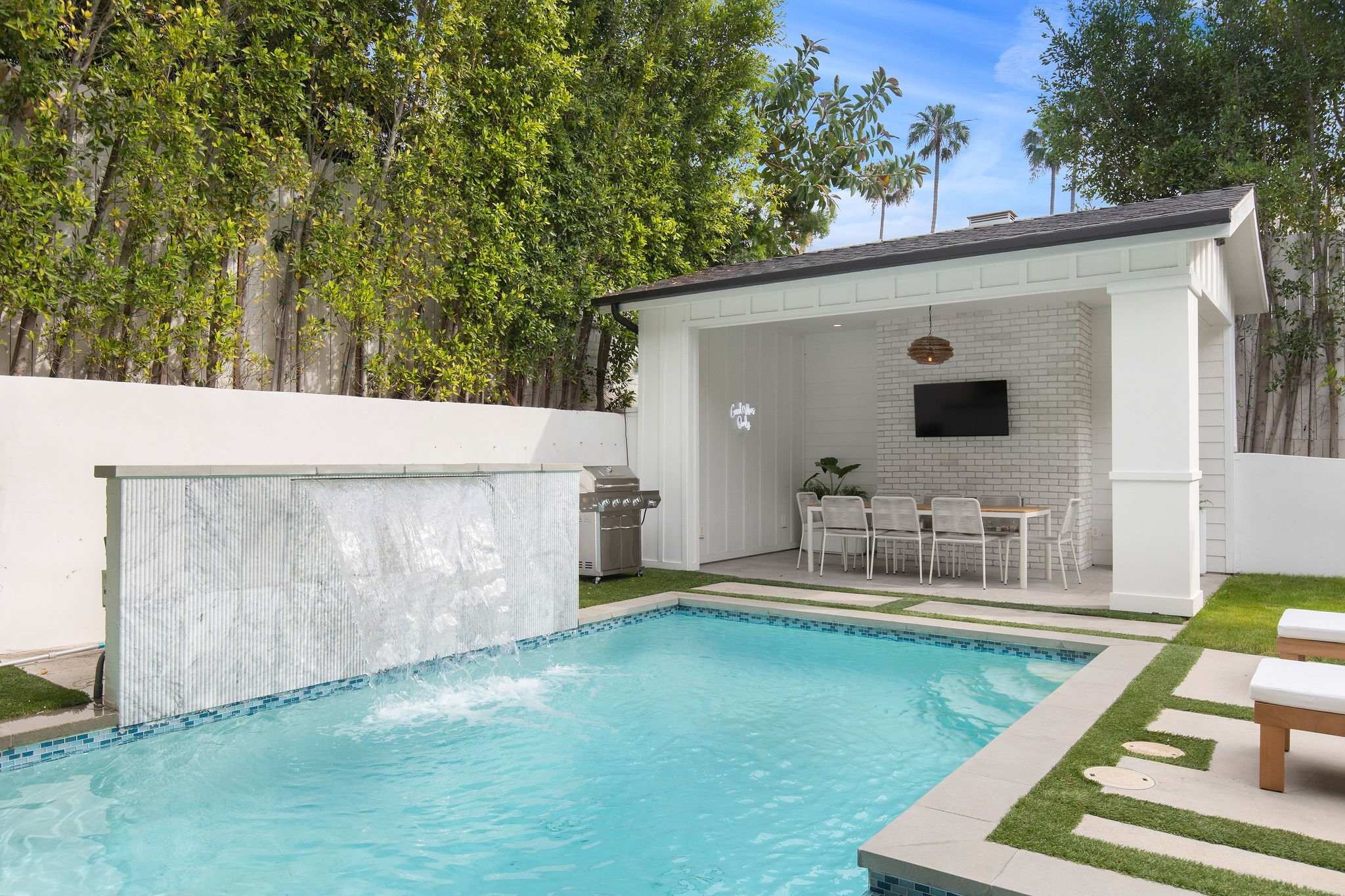 A luxury pool and spa with waterfall feature, cabana, and built-in outdoor bar area