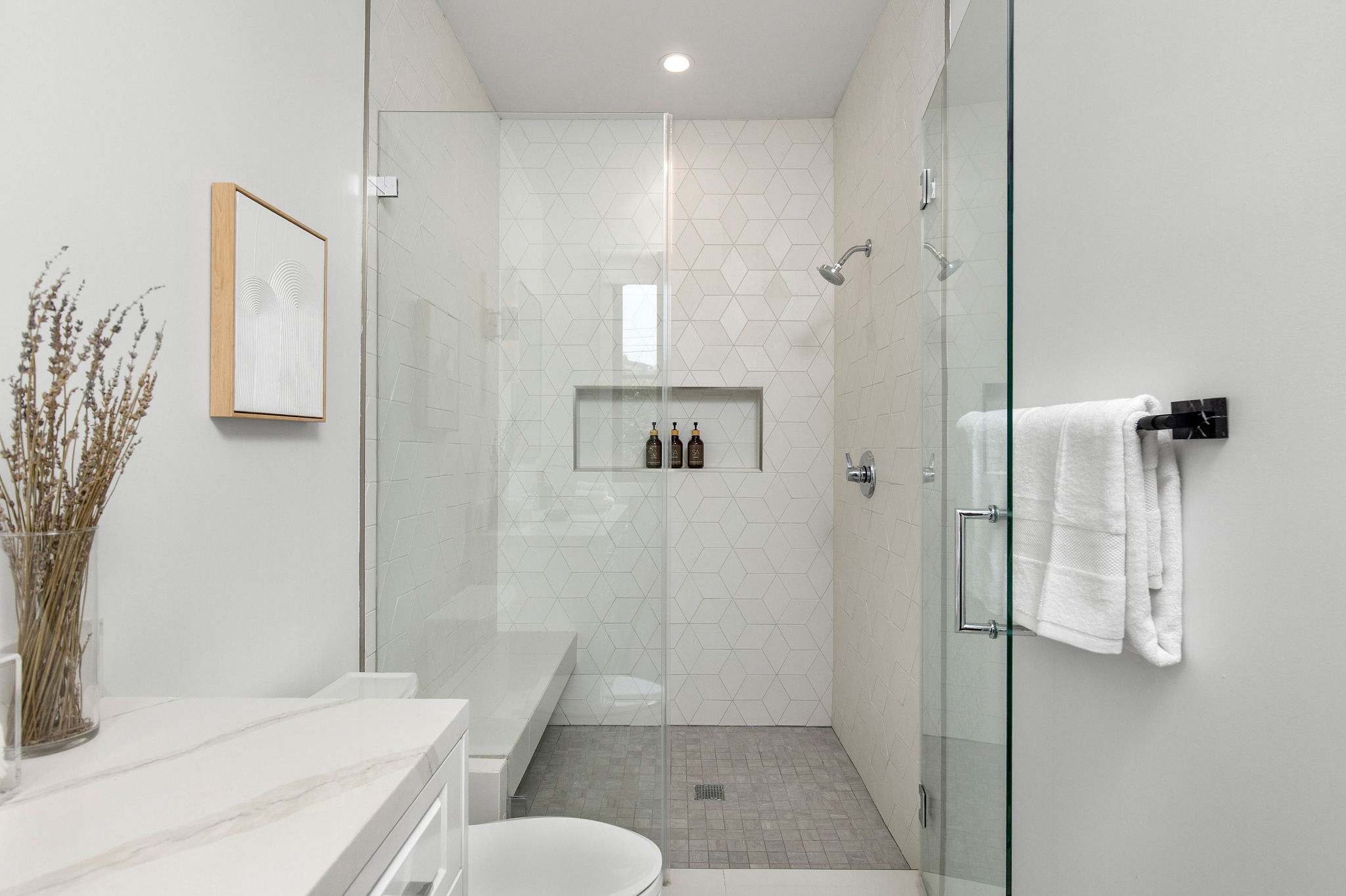 A walk-in shower designed with full-height tile, glass enclosure, and built-in niche shelving