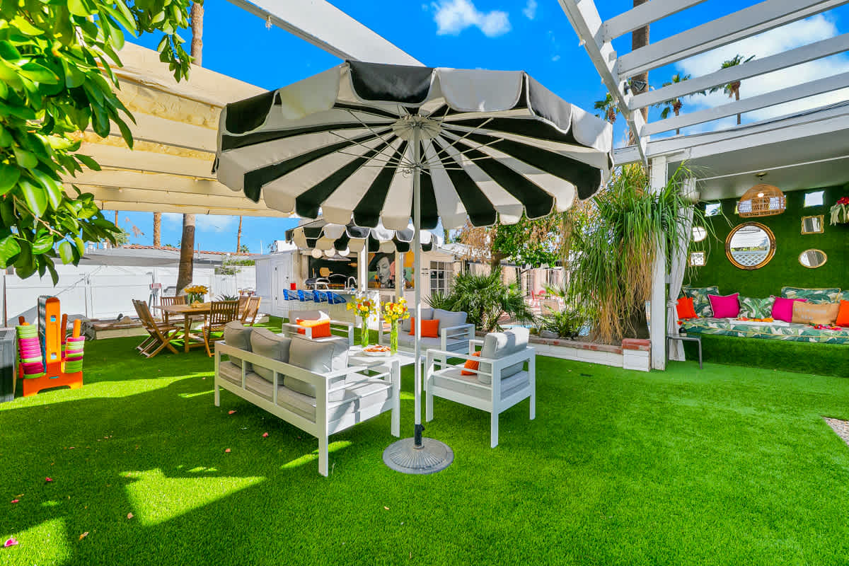 Outdoor dining on green lawn beneath striped umbrellas and a white pergola.