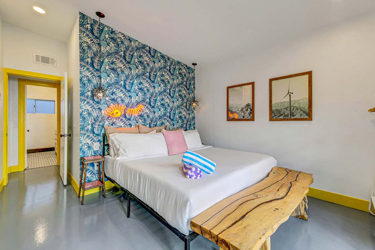 Bedroom with a blue leaf-patterned accent wall, white bedding and a wooden bench.