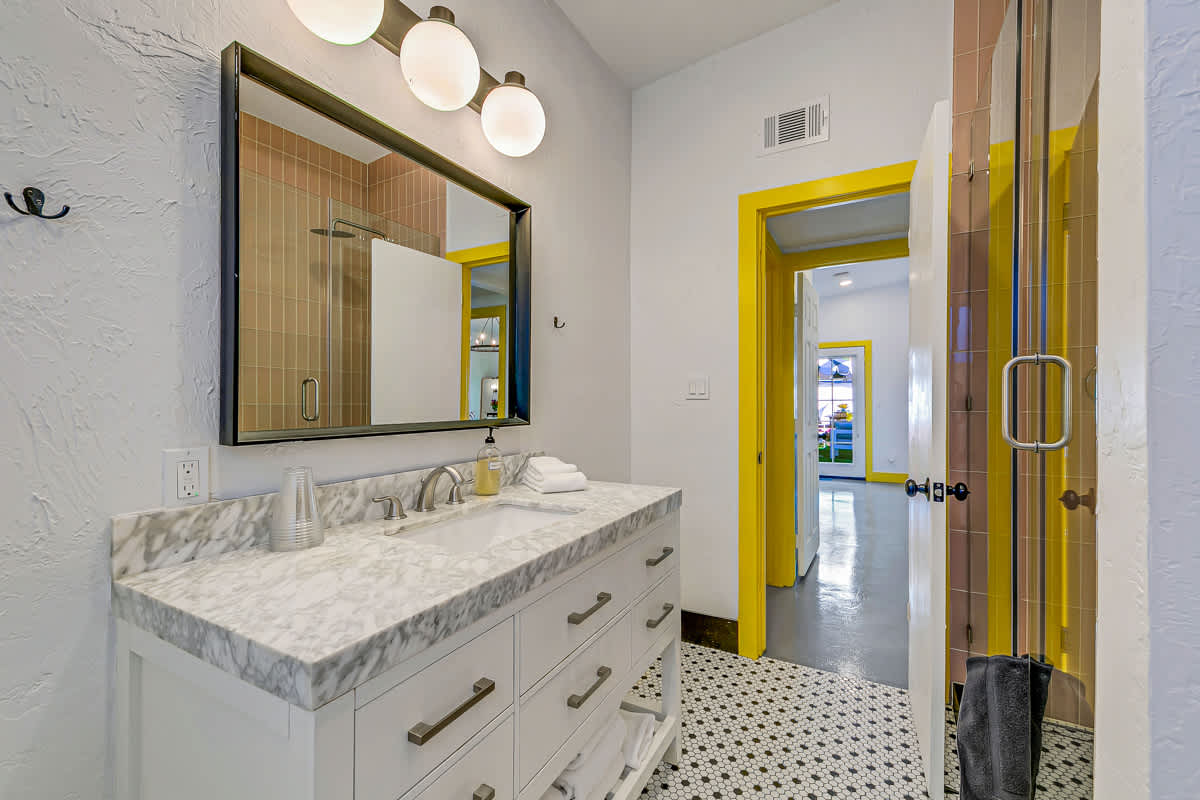 White vanity with a stone-look countertop, wall mirrors and yellow-trimmed doorway.