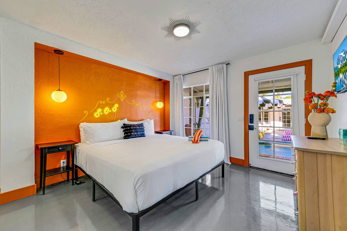 Orange-accent bedroom with a wooden bench and glass doors opening outside.