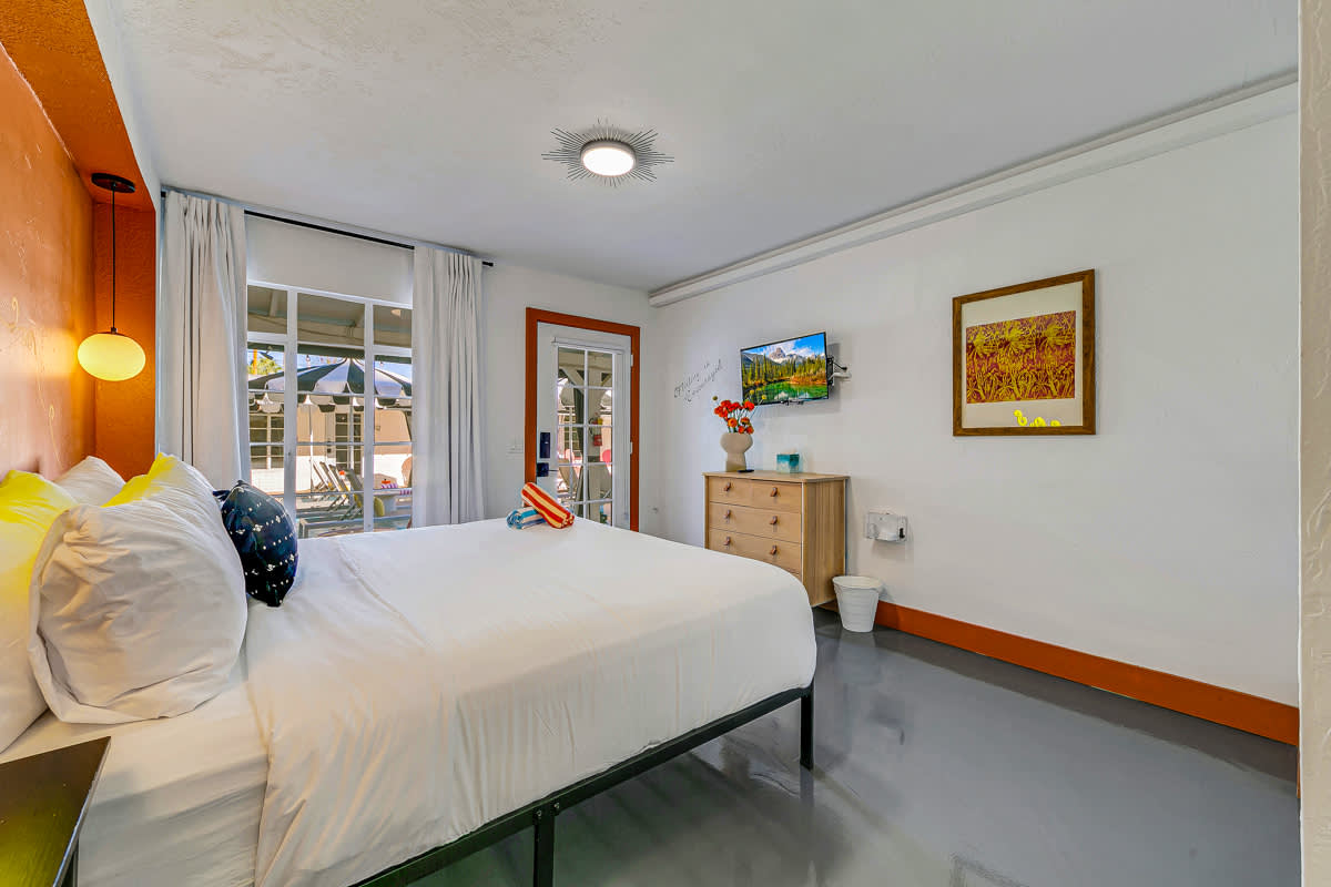 Bedroom view toward the glass doors, framed artwork and bedside seating.