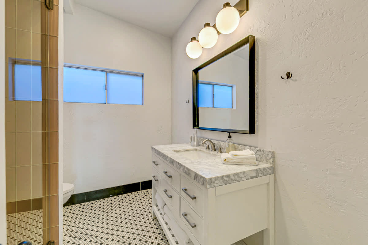 Bathroom vanity with a framed mirror, globe lights and a tiled shower.