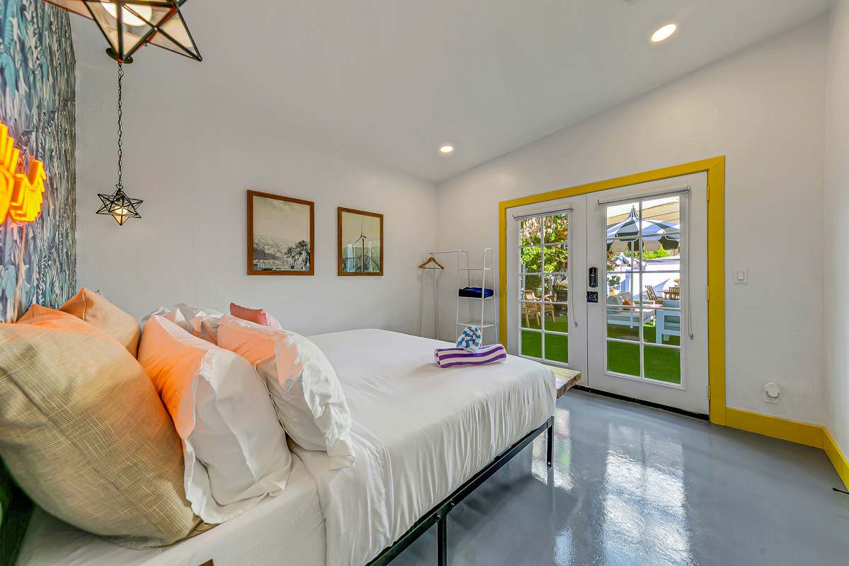 Bedroom with patterned wallpaper, white bedding and a glass door to the courtyard.