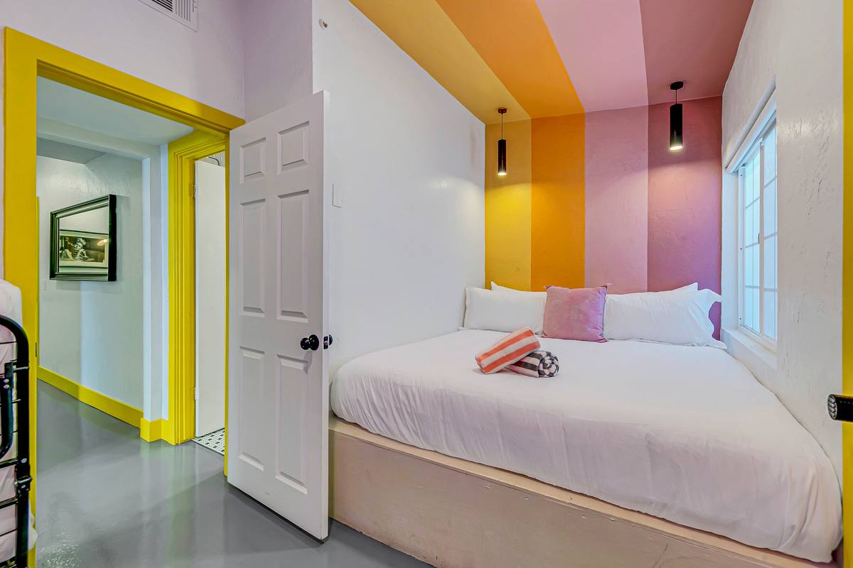 Sleeping nook with a low bed, white bedding and colorful ceiling panels.