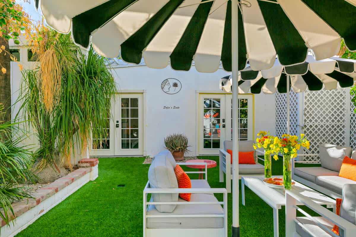 Outdoor dining furniture beneath a striped umbrella beside the garden path.