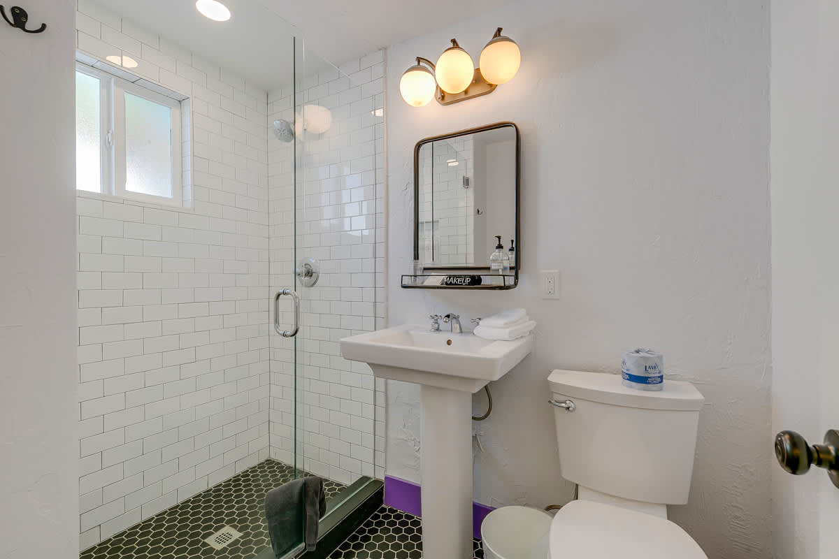 Bathroom with a pedestal sink, toilet, wall mirror and white tiles.