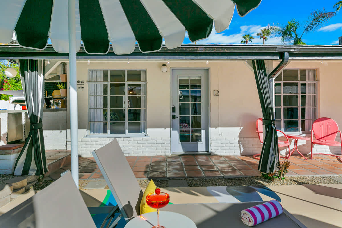 Outdoor dining table and white chairs beneath a green-and-white striped umbrella.