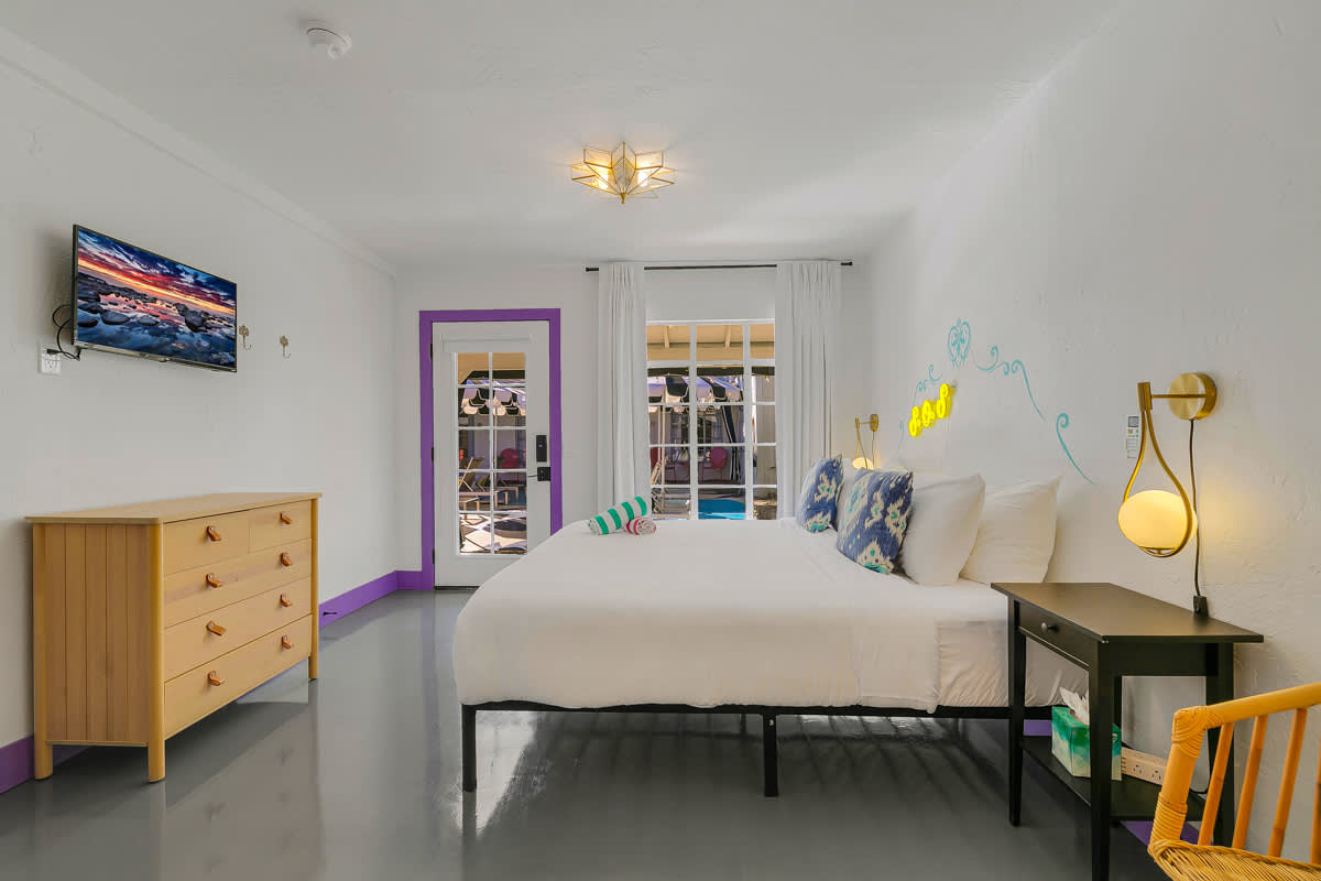 Bedroom with a wall-mounted television, wood dresser and purple-trimmed doorway.