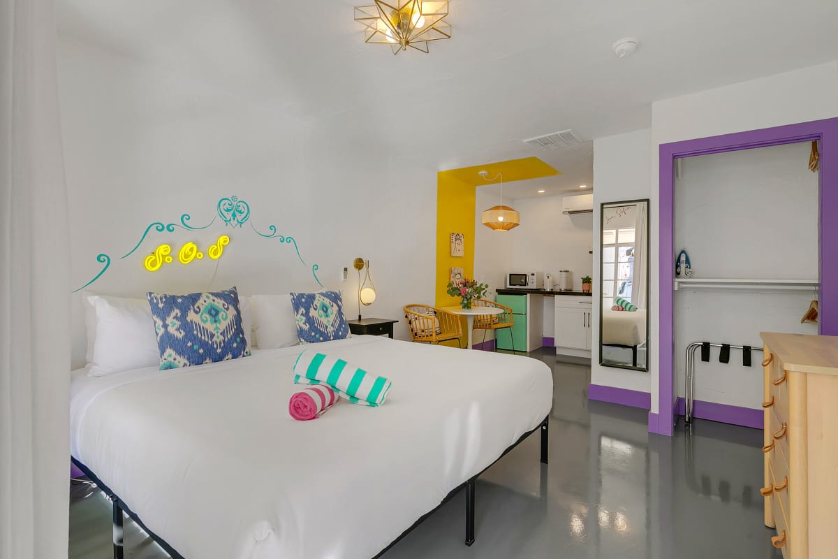 White bed with patterned pillows, yellow trim and a purple-framed doorway.