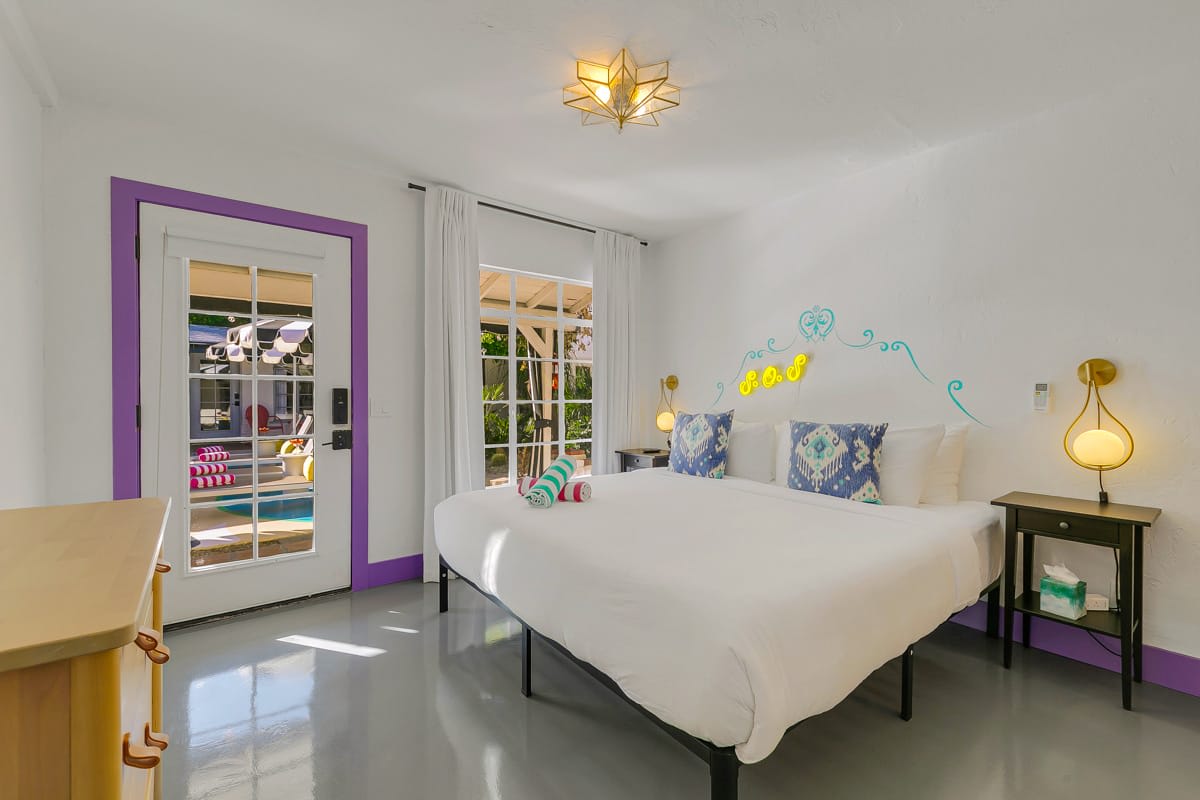 Wide bedroom view with white bedding, dresser and glass doors opening outside.