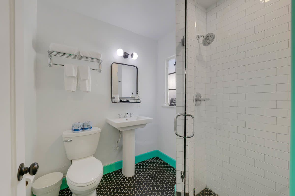 White-tiled bathroom with a pedestal sink, toilet and mint-green doorway.