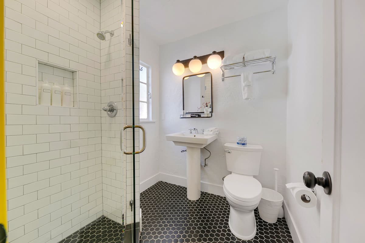 Bathroom with a walk-in shower, pedestal sink, toilet and dark mosaic floor.