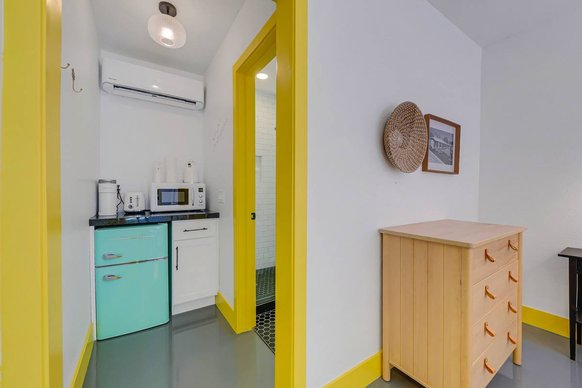 Wood dresser and yellow-trimmed hallway leading to a mint-green kitchenette.