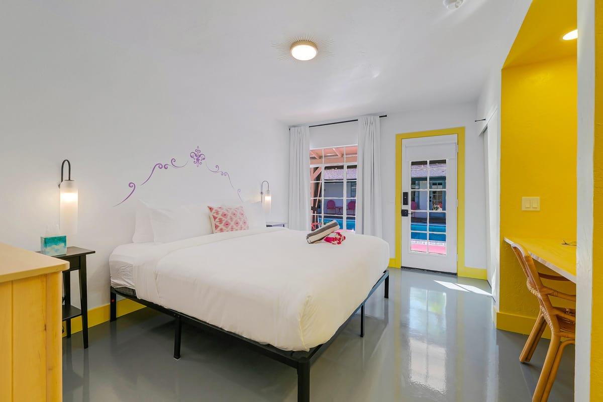 Wide bedroom view with yellow trim, glass doors, open clothing storage and a chair.