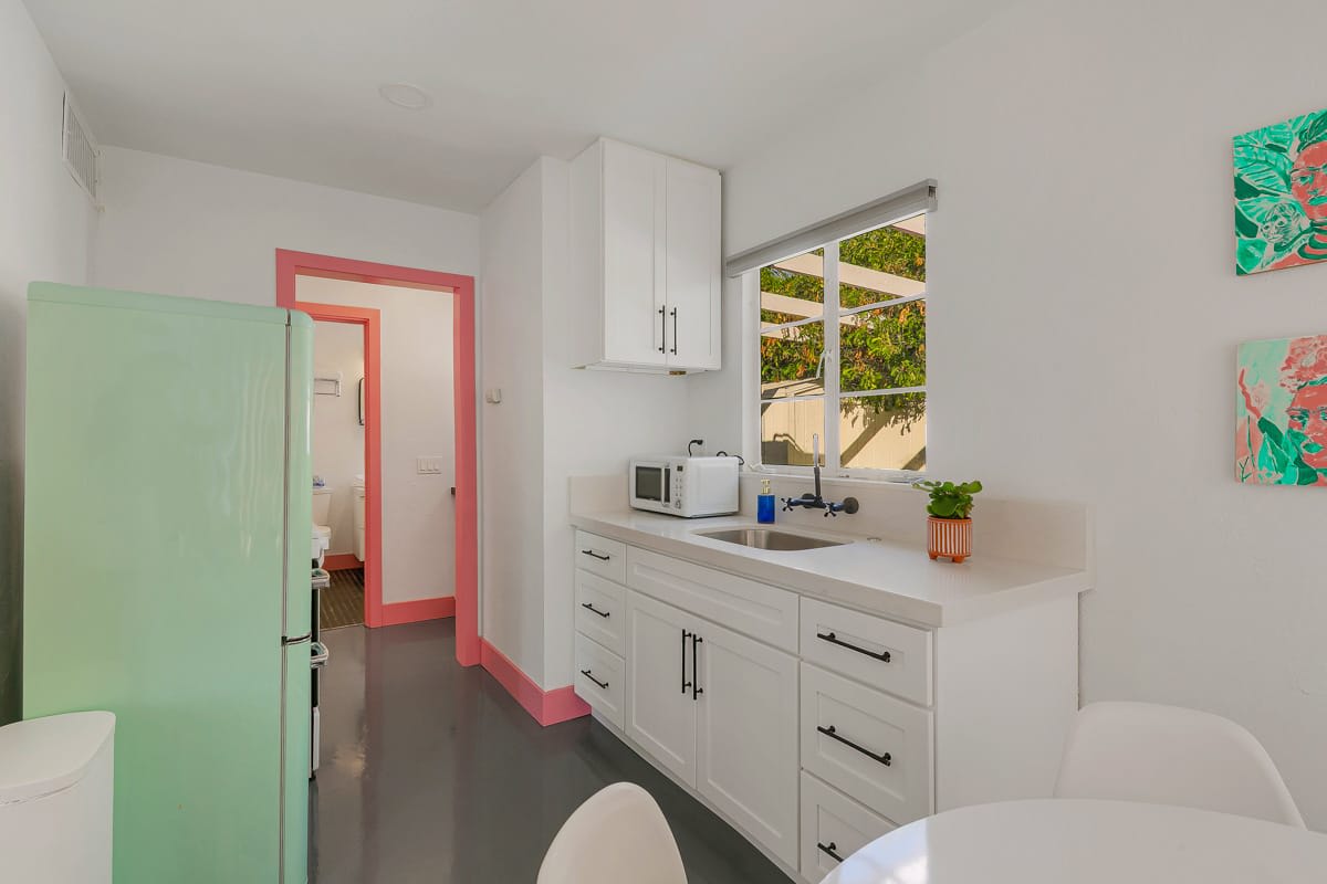 White kitchen counters and cabinets with a garden window and pink doorway.
