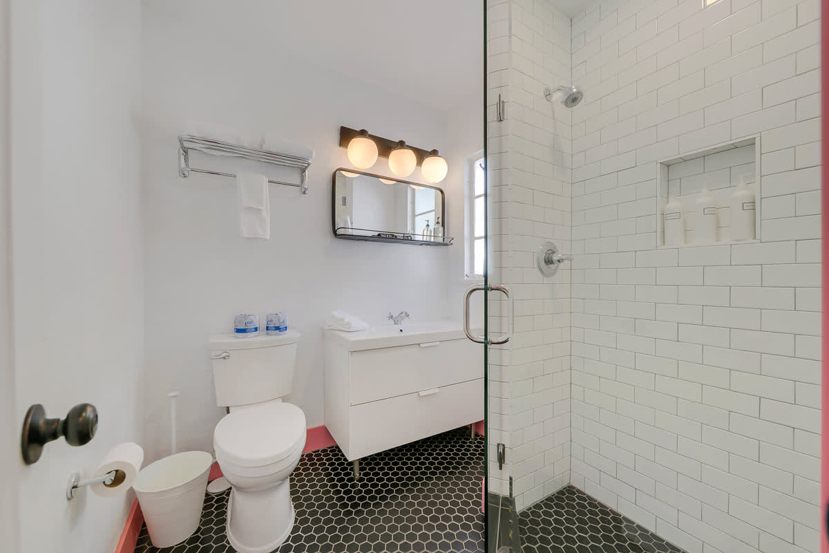 White-tiled bathroom with a walk-in shower, pedestal sink and toilet.