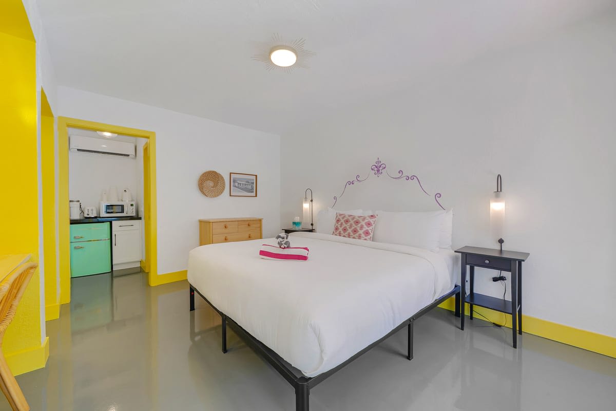 White bed with bedside tables in a yellow-and-pink-accent room.