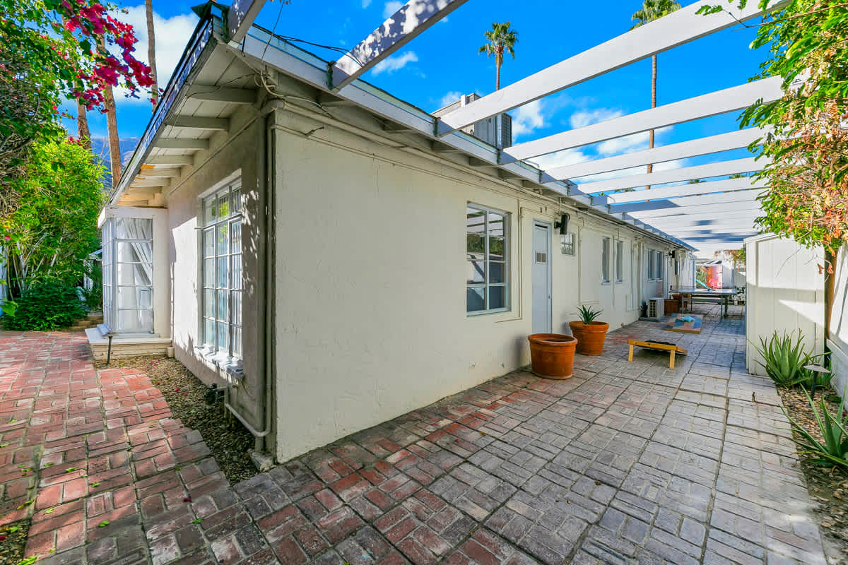 Paved side passage beneath an open pergola alongside the white building.