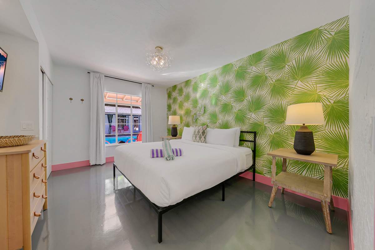 Bedroom with green patterned wallpaper, a wood dresser and pink-trimmed doorway.