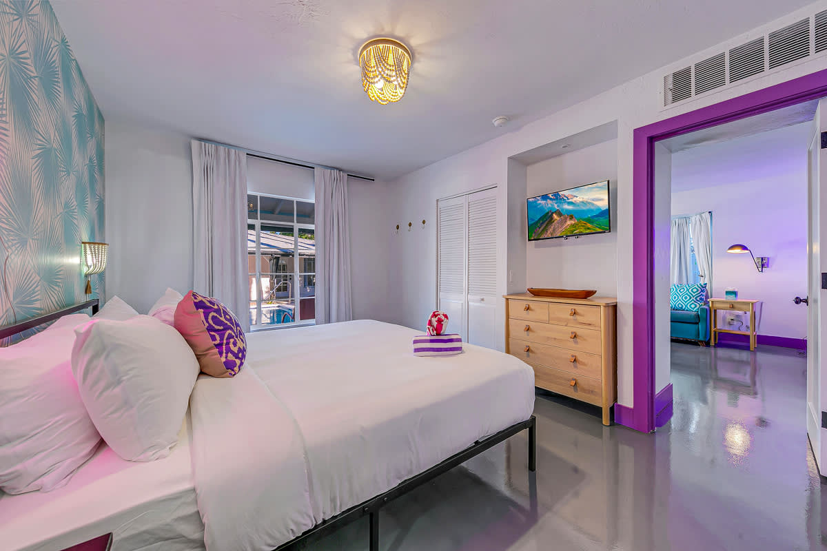 Bedroom with a blue patterned wall, white bedding and purple trim.