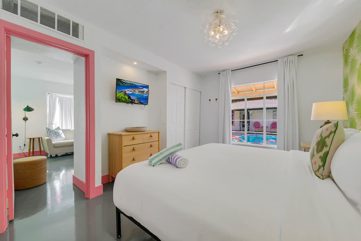 Bedroom view toward a wall-mounted television, dresser and pink-framed doorway.