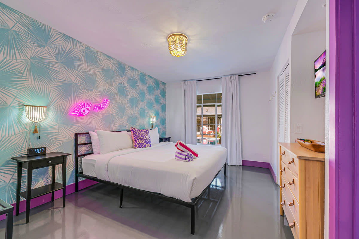 Bedroom with patterned wallpaper, bedside lamps and a purple-framed doorway.