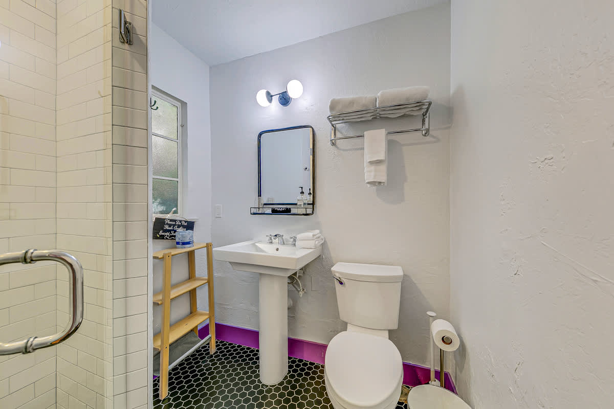 White-tiled bathroom with a pedestal sink, toilet and purple doorway.