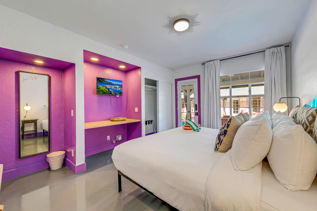 Bedroom with purple accents, a wall-mounted television and a wooden dresser.