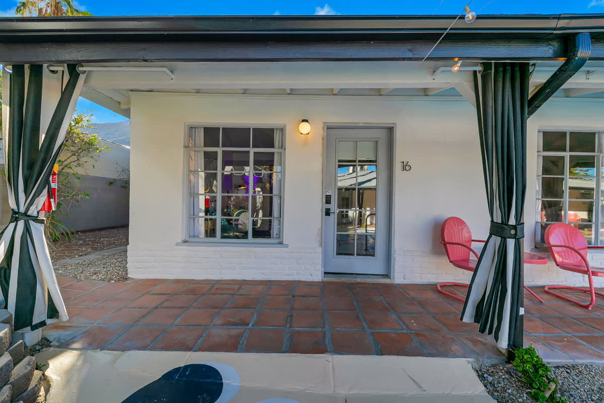 Exterior of a poolside room with French doors, awning and pink chairs.