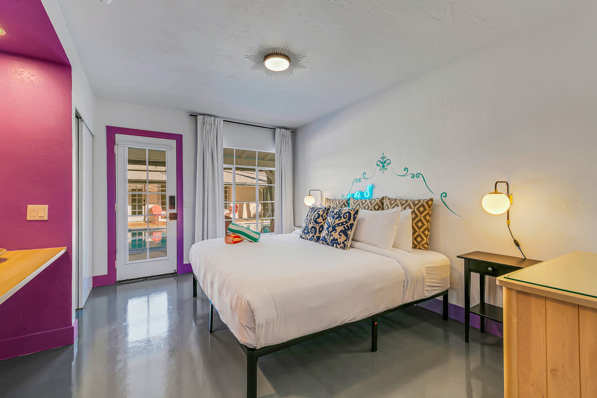 White bed and bedside furniture beside a purple-trimmed doorway.