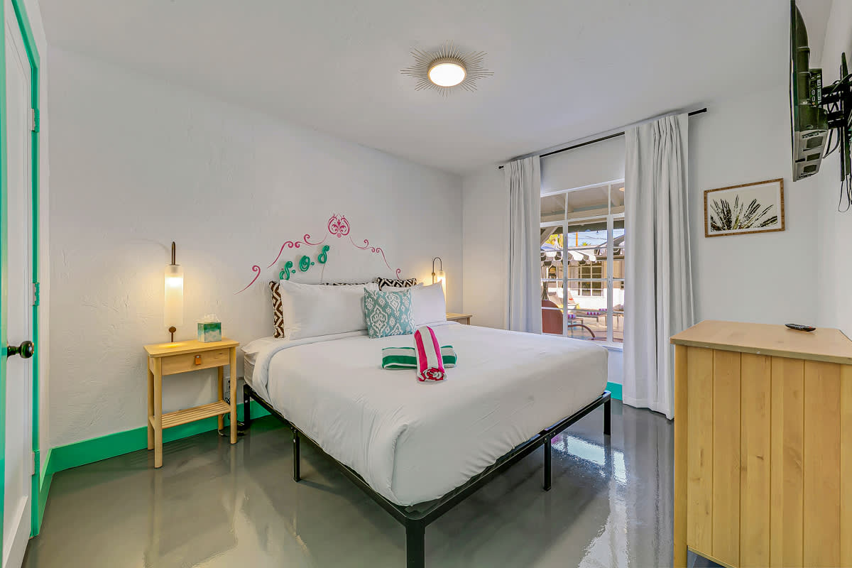 White bed in a mint-trimmed room with a television and wooden dresser.