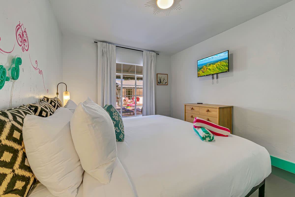 Bedroom with white bedding, mint-green trim and a wall-mounted television.