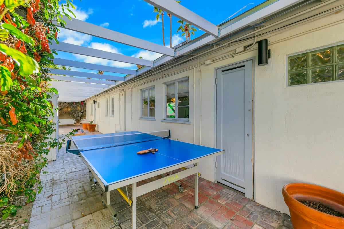 Outdoor table-tennis table in the paved passage beneath an open pergola.