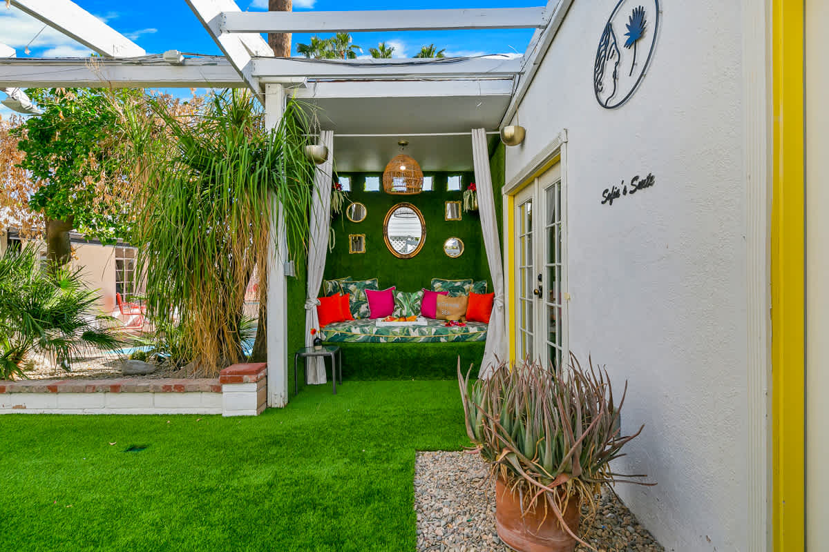 Garden walkway and lawn beneath a white pergola beside outdoor seating.