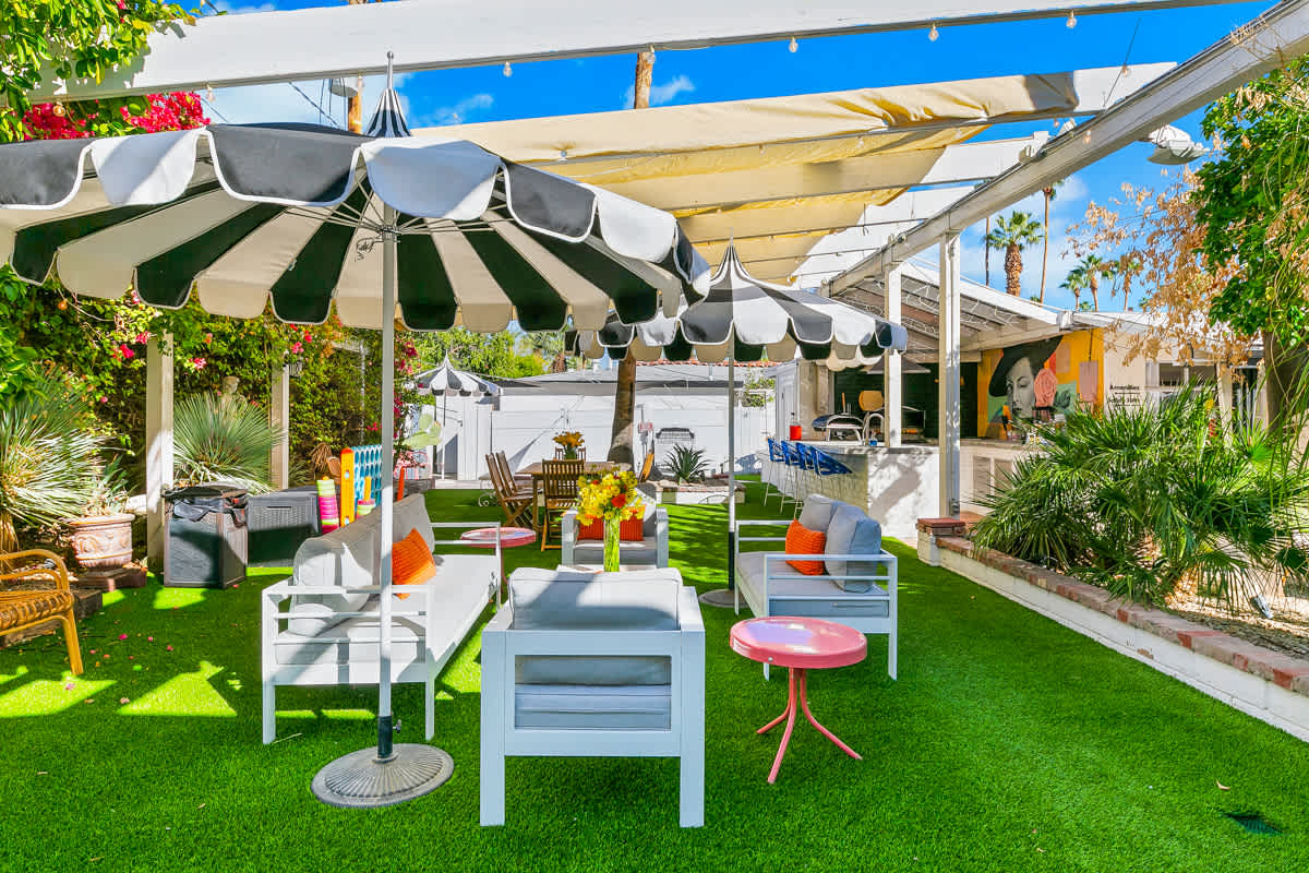 Wide outdoor dining area on lawn beneath striped umbrellas and a white pergola.
