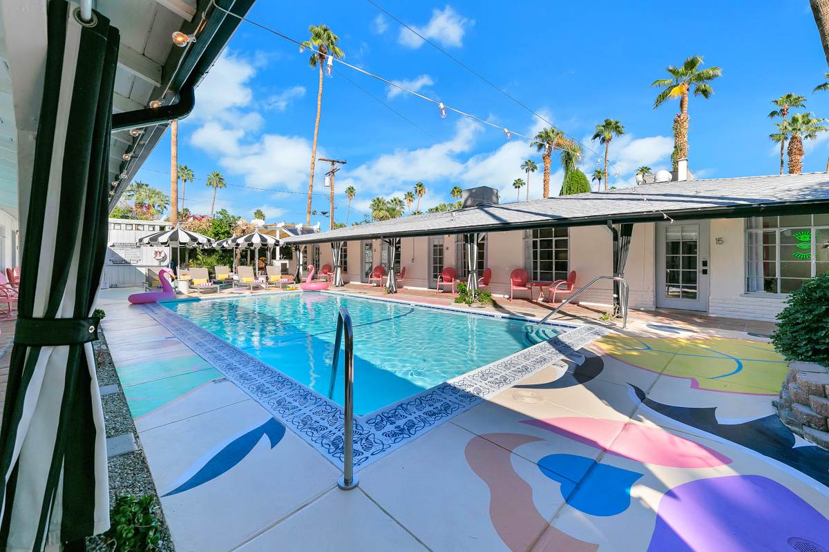 Poolside rooms and rectangular swimming pool beneath tall palm trees.