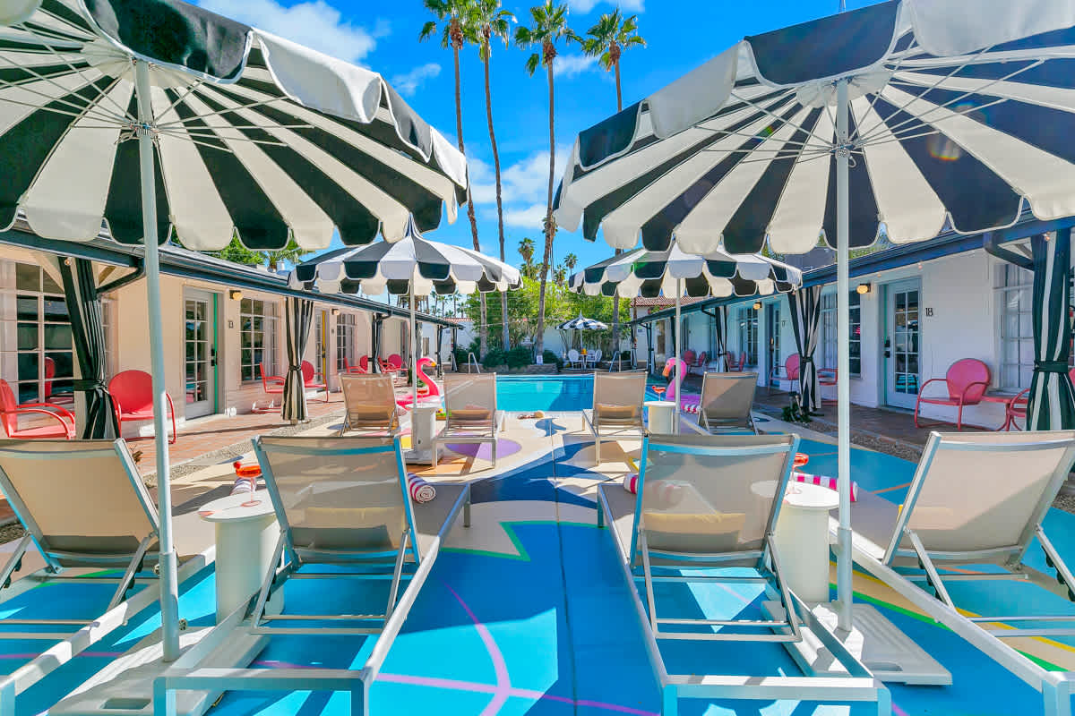Poolside lounge chairs beneath striped umbrellas with courtyard rooms beyond.